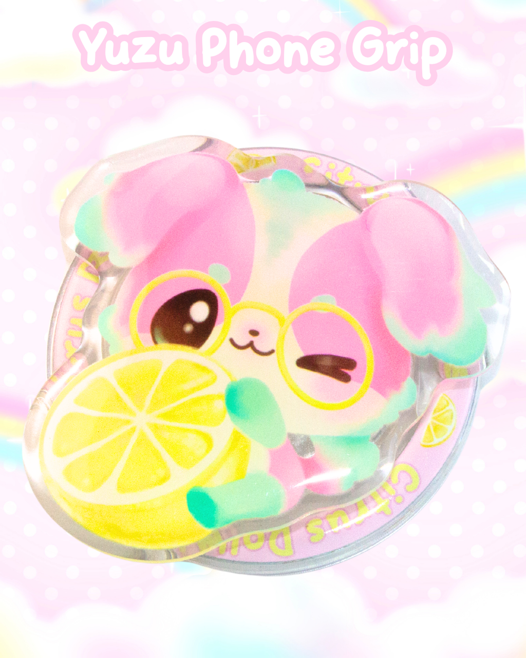 A pastel pink and mint green  phone grip featuring a cute cartoon dog character wearing glasses and holding a lemon slice, set inside a clear circular frame. The text 'Yuzu Phone Grip' is written at the top against a soft pink background with a faint rainbow.